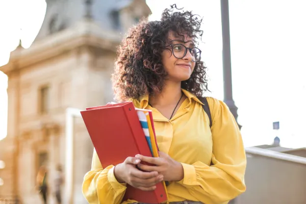 girl in yellow shirt holding books standing in front of a university building