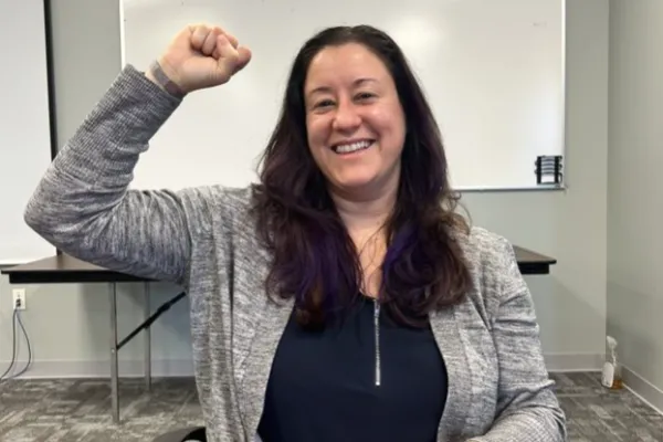 Our member in a conference room smiling at the camera with her fist raised 