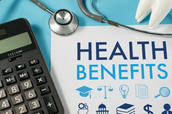 A calculator, stethoscope, and piece of paper that reads "Health Benefits" overlayed on blue background 