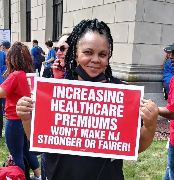 CWA Member holding sign that reads "increasing healthcare premiums won't make NJ stronger or fairer!"